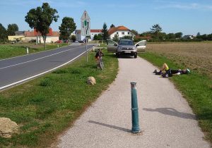 Poller mit dem verletzten Radler am Boden liegend. Dahinter ein Auto eines Helfers. Foto: Radlobby NÖ